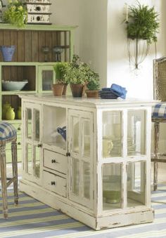 an old white cabinet with glass doors in a room filled with potted plants and furniture