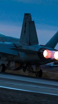 a fighter jet taking off from an airport runway at night with lights on it's wings