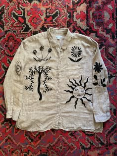 a white shirt with black designs on it sitting on top of a red and blue rug