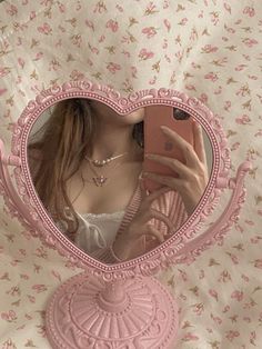 a woman taking a selfie in front of a pink heart shaped mirror with flowers on it