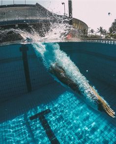 a person swimming in a pool with blue water and splashing from the side,