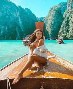 a woman is sitting on the bow of a boat in front of mountains and water