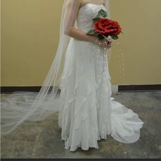 a woman in a white wedding dress holding a red rose and veil over her head