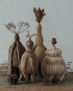 three clay sculptures sitting next to each other on a wooden table with plants and pine cones