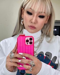 a woman with blonde hair holding a pink cell phone in her right hand and looking at the camera