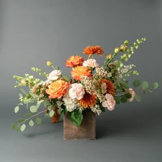 an arrangement of flowers in a wooden vase on a gray background with greenery and leaves