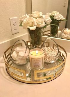 a candle and some flowers in a vase on a tray with mirrors behind it that is sitting on a bathroom counter