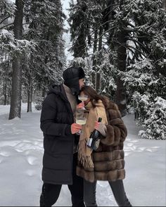 a man and woman standing next to each other in the snow holding bottles of wine