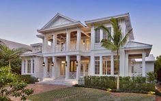 a large white house with lots of windows and palm trees in the front yard at dusk