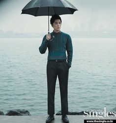 a man holding an umbrella while standing next to the water in front of him on a cloudy day