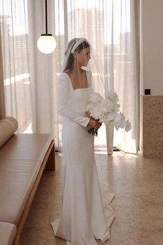 a woman in a wedding dress holding a bouquet of flowers and looking out the window