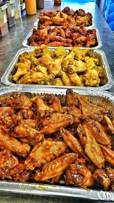 three tin trays filled with different types of chicken wings and other foods on top of a table