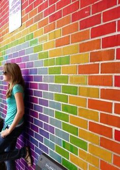 a woman leaning against a colorful brick wall