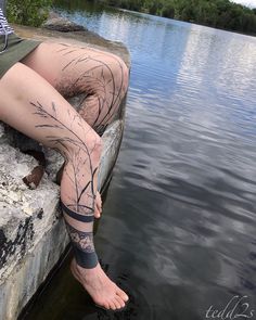 a woman sitting on top of a rock next to a lake with her legs crossed