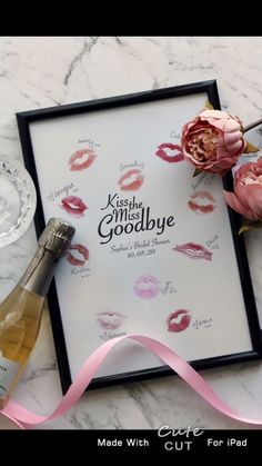 a bottle of wine and some pink flowers on a marble table with a framed sign that says kiss me goodbye