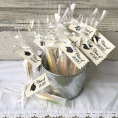 graduation party favors in a bucket on a white tablecloth with ribbons and tags attached to them