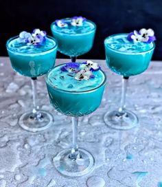 three martini glasses filled with blue liquid and garnished with flowers on the rim