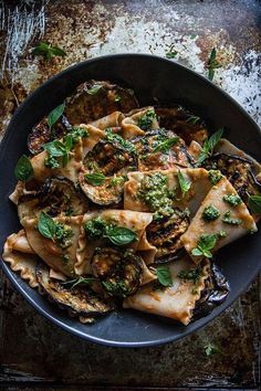 a black plate topped with ravioli covered in pesto