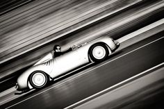 a silver race car driving down a track with blurry lines in the back ground