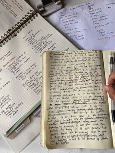 an open notebook with writing on it and a hand holding a pen next to it