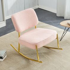 a pink rocking chair sitting on top of a rug next to a table and books