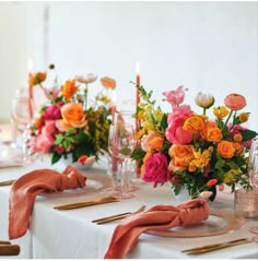 the table is set with pink and orange flowers, gold place settings and napkins