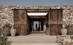 an open door leading into a stone building with cactus in the foreground and two people standing outside