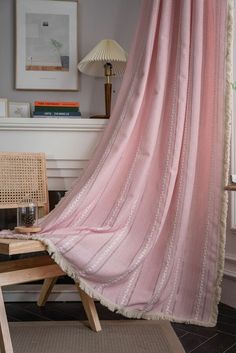 a pink curtain hanging from the side of a wooden chair next to a table with a lamp on it