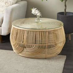 a wicker coffee table with glass top in front of a white couch and potted plant