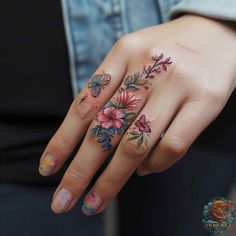 a woman's hand with flowers and butterflies tattooed on her fingers, holding onto the ring