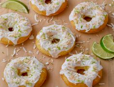 several donuts with white frosting and toppings on a wooden board next to lime wedges