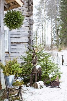 a log cabin in the woods with snow on the ground and evergreens hanging from it's roof