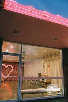 a pink neon sign on the side of a building with a bench in front of it