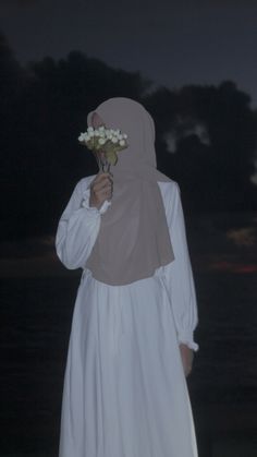 a woman in a white dress holding a flower up to her face with the night sky behind her