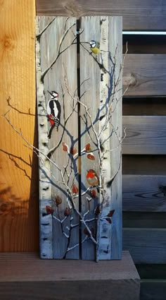 a wooden panel with birds and branches painted on it, next to a wood fence