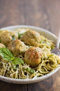 a white bowl filled with spaghetti and meatballs covered in pesto sauce on top of a wooden table