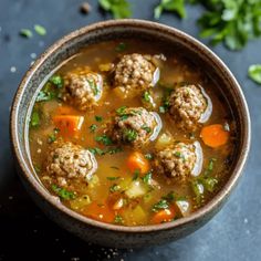 a bowl filled with meatballs and vegetables on top of a table next to some parsley