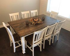 a dining room table with white chairs and a wooden centerpiece on top of it