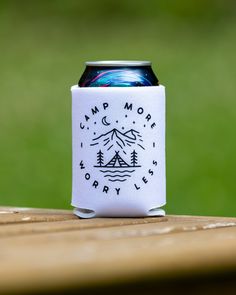 a can cooler sitting on top of a wooden table next to a green grass field