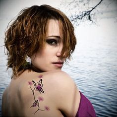 a woman with a tattoo on her back standing in front of the water and looking off into the distance