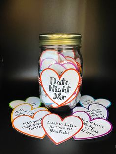 a jar filled with lots of hearts sitting on top of a black table next to tags