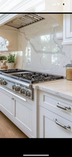 a kitchen with white cabinets and marble counter tops, along with an open range hood