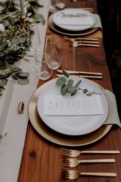 the table is set with plates, silverware and greenery