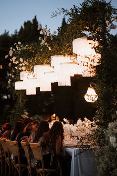 a group of people sitting at a dinner table under paper lanterns hanging from the ceiling