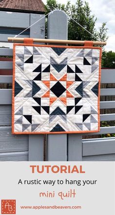 an orange and black quilt hanging on a fence with text overlay that reads,'how to make a rustic way to hang your mini quilt