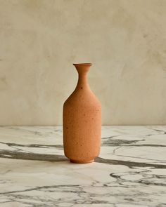 a brown vase sitting on top of a white marble counter next to a beige wall