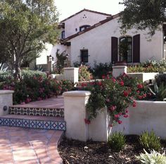 a white house with red flowers in the front yard and steps leading up to it