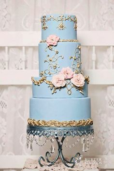 a blue and gold wedding cake with pink flowers on the top tier is sitting on a table