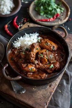 a pan filled with meat and rice on top of a wooden cutting board next to other dishes