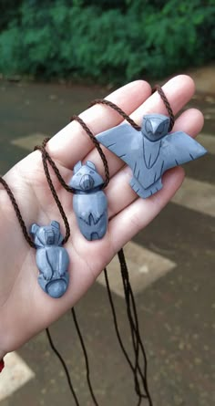 a hand holding three small clay animals on string attached to it's palm, with trees in the background